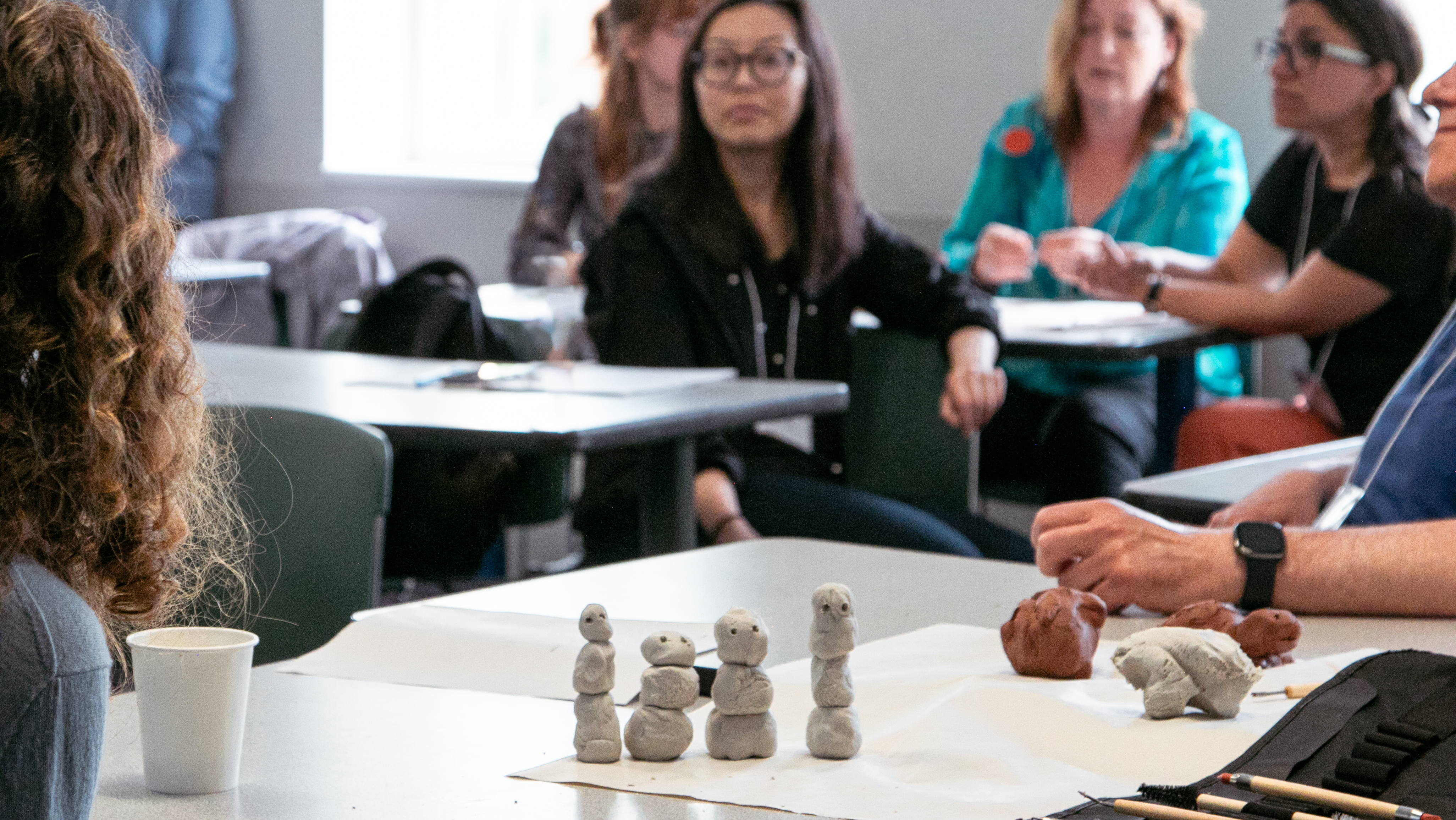 Four clay snowman-shapred figures sit on a desk while participants look on in the background.