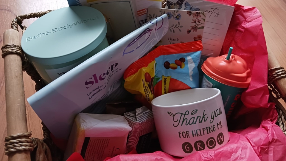 A gift basket containing a candle, bath salts, candy and stationary.