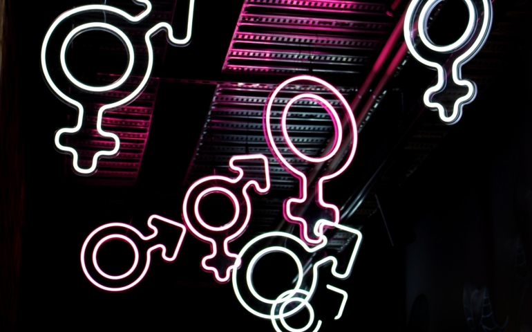 A collage of neon gender symbols float on a dark background 